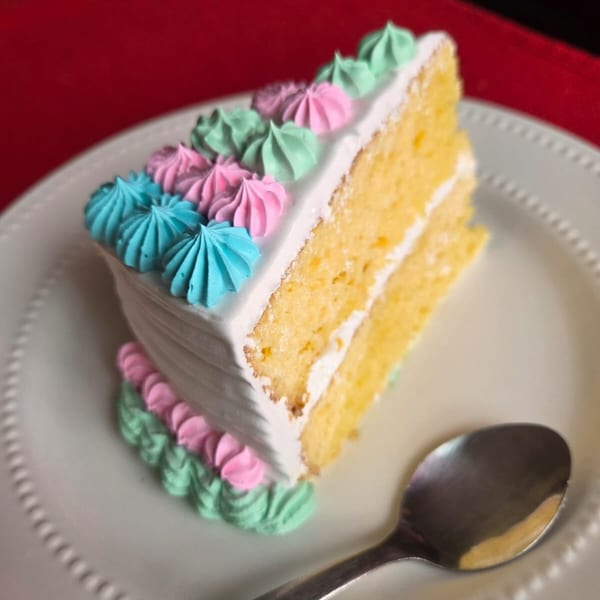 Slice of vanilla cake with white frosting and colorful pink, blue, and green meringue decorations.