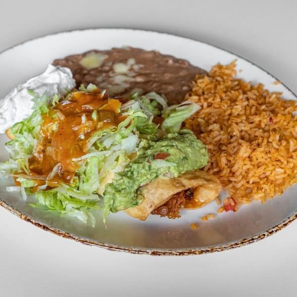 Mexican combination plate with a crispy taco, refried beans, rice, guacamole, sour cream, and salsa.