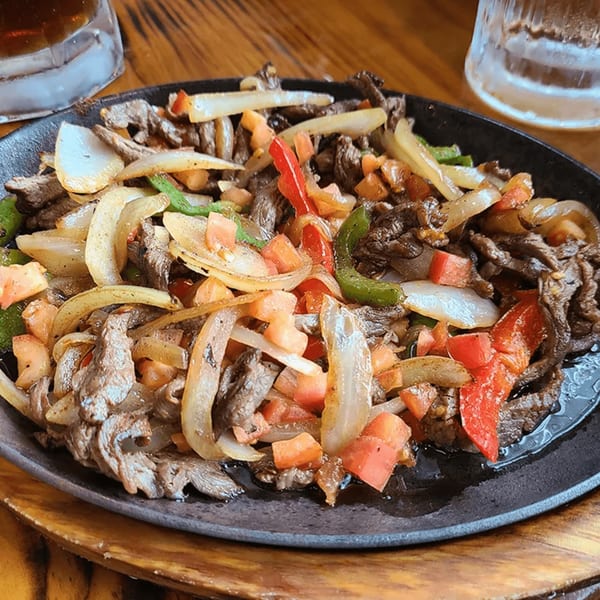 Sizzling beef fajitas with onions, red and green bell peppers, and diced tomatoes on a black platter.