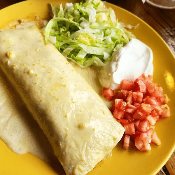 A La Calera Mexican Bar & Grill burrito covered in white sauce, with lettuce, sour cream, and diced tomatoes.