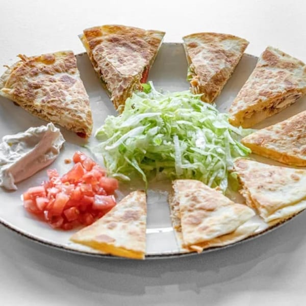 A plate of La Calera Mexican Bar & Grill quesadilla wedges with shredded lettuce, diced tomatoes, and sour cream.