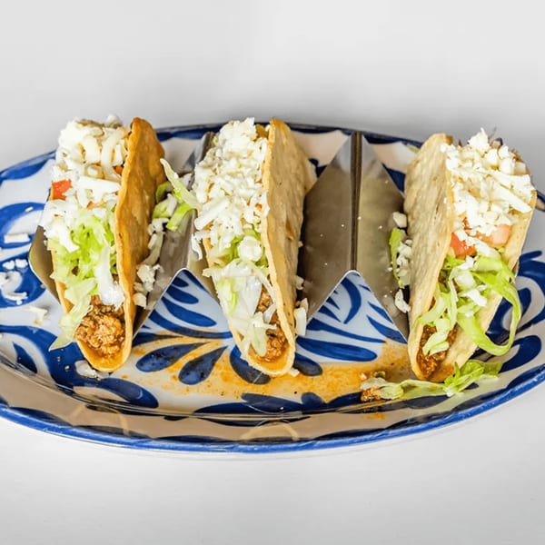 Three La Calera Mexican Bar & Grill tacos with meat, lettuce, and cheese on a decorative plate.