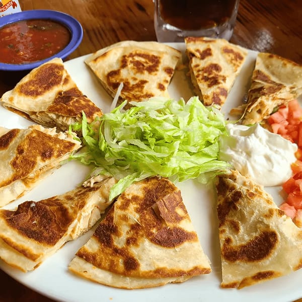 A plate of La Calera Mexican Bar & Grill quesadillas with lettuce, sour cream, diced tomatoes, and salsa.