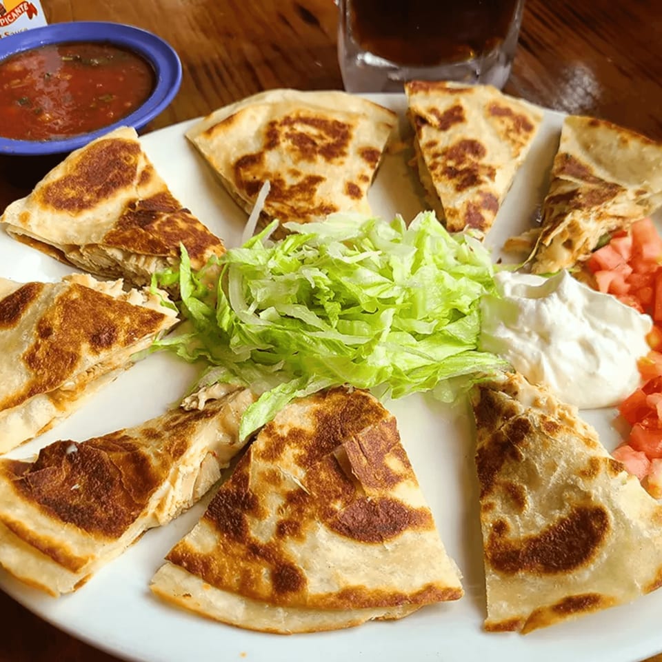 A plate of La Calera Mexican Bar & Grill quesadillas with lettuce, sour cream, diced tomatoes, and salsa.