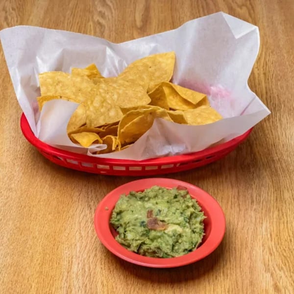 A red basket of tortilla chips and a red bowl of guacamole on a wooden table.
